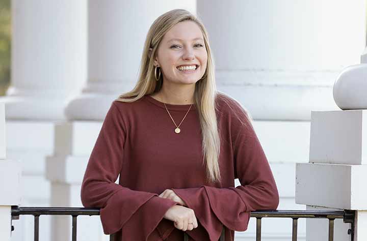 Madison Hobbs stands on porch and smiles for the camera.