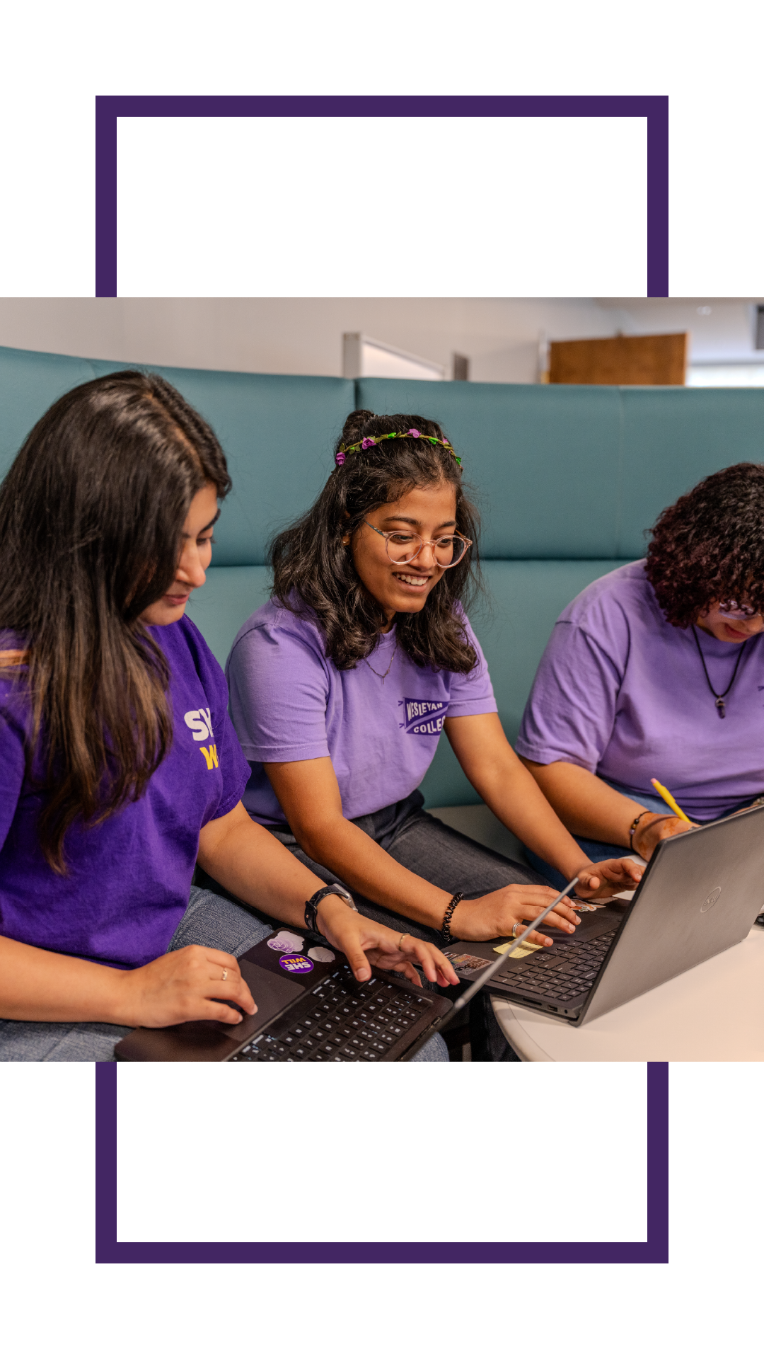 Three students wearing purple Wesleyan shirts sit together using laptops and writing notes in a collaborative indoor study space.