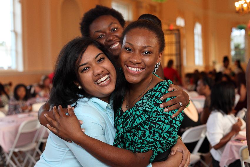 Three students hug and laugh.