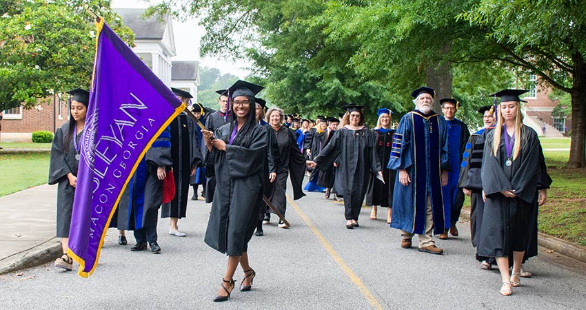 Students in regalia march with the Wesleyan Flag