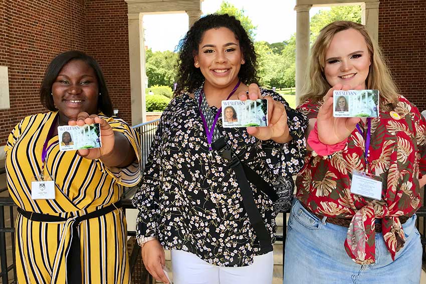 Three students hold their student IDs