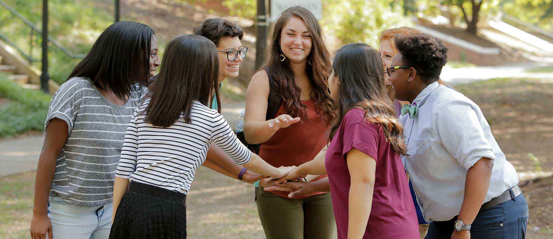 Students stand in circle facing each other outside in the quad