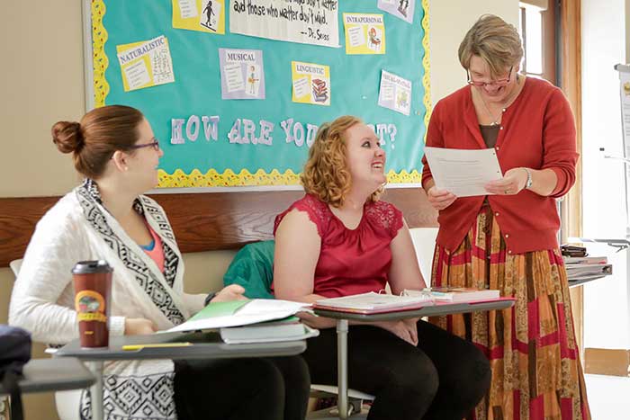 Education instructor looks over students paper in classroom.