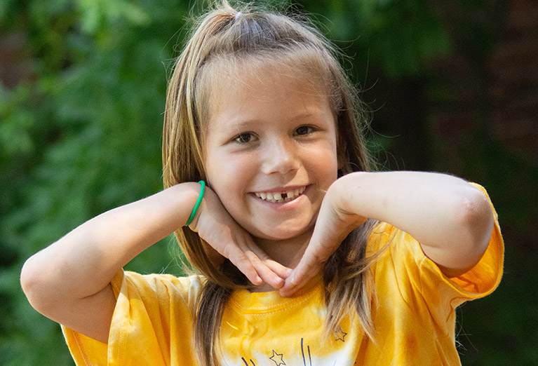 Kid's College camper smiles for the camera outside.