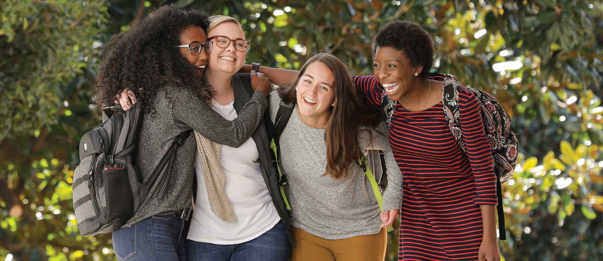 Four students laugh and hug while walking outside.